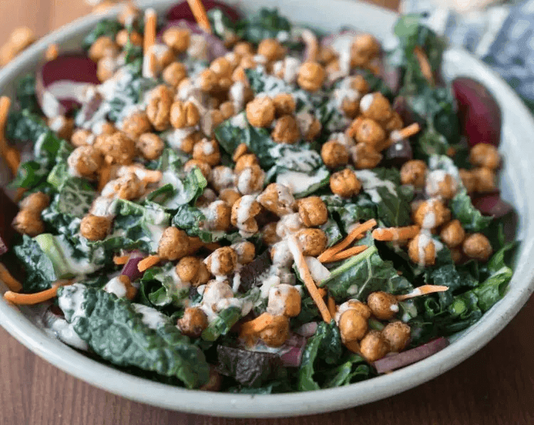 Breakfast bowl of roasted chickpeas, kale, carrots, and tahini drizzle—offering chickpeas as a hearty alternative protein source.