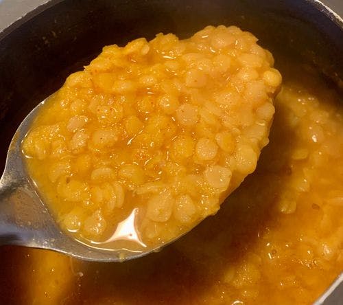 A spoonful of boiled yellow lentils over a pressure cooker.
