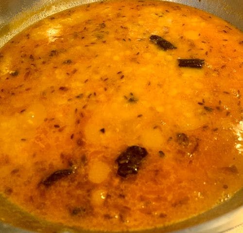 Cooked yellow lentils with specks of cumin and pieces of broken red chilli on top.