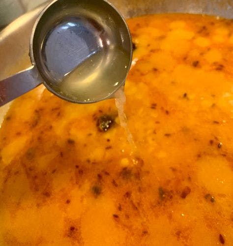 Lemon juice being poured from a measuring spoon into a pan full of cooked yellow lentils.