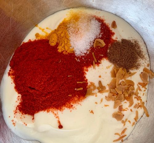 Whisked yogurt with whole and powdered spices in a mixing bowl