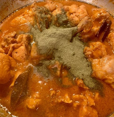 Green mint powder poured on orange chicken curry