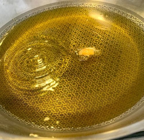 Oil in a heavy-bottomed pan with a piece of bread on the surface indicating the oil is ready for frying. 