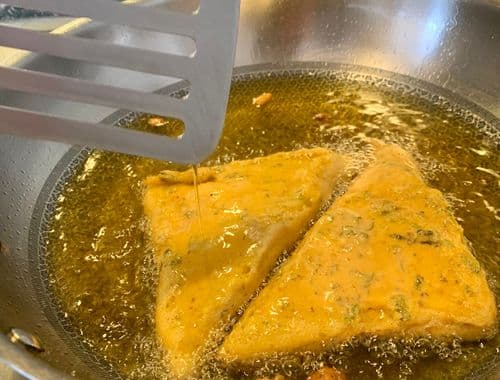 2 triangular slices of dipped bread being fried in oil