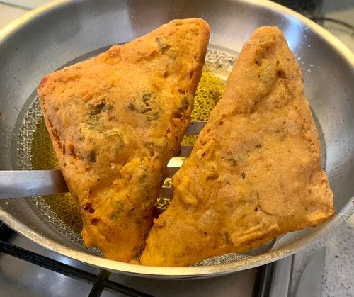 2 pieces of cooked bread pakora resting on a flat-slotted spatula.