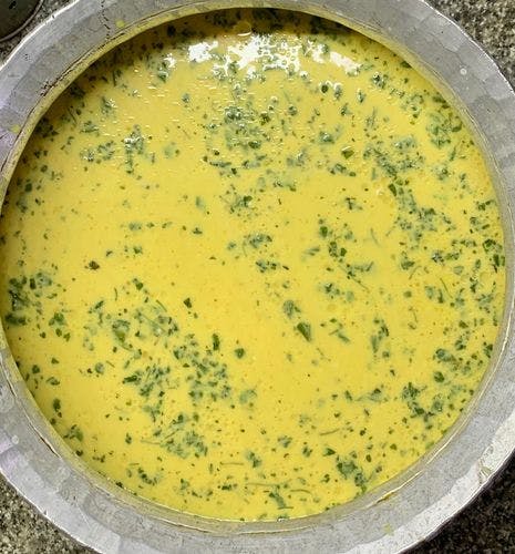 Yellow kadhi mixture with speckles of green herbs in a pot