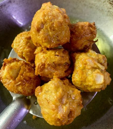 A bunch of fried fritter balls resting on a slotted spatula