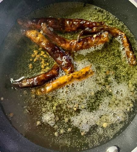 Dry red chillies and other spices being fried in oil. 