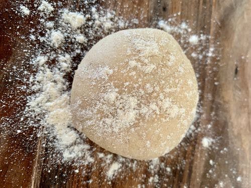 Dough ball dusted with flour on a wooden board.