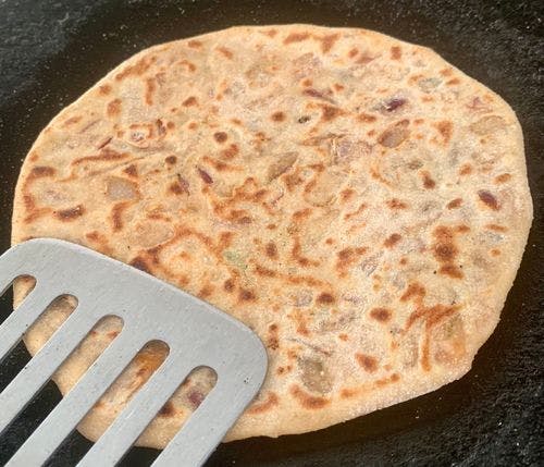 Flat steel ladle on a partially cooked paratha