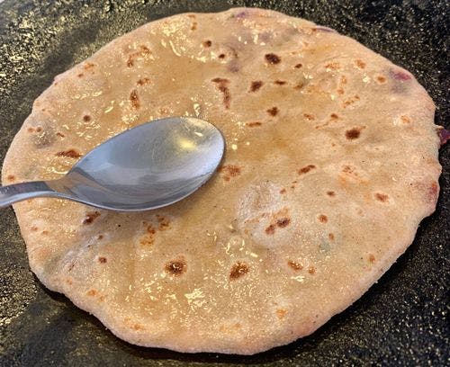 Oil in a tablespoon on a partially cooked paratha