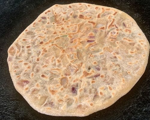 Partially cooked round paratha on a pan.