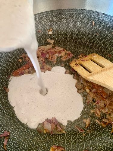 White liquid being poured on to chopped onions and spices in a pan.