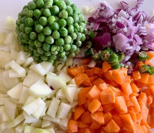 Chopped potatoes, carrots, onions, green chillies and peas on a wooden board. 
