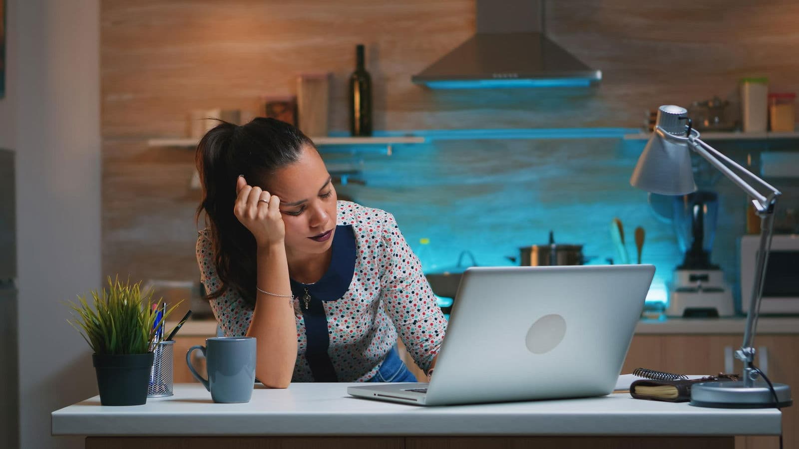 Food content creator looking exhausted while working in the kitchen, surrounded by cooking tools and a laptop.