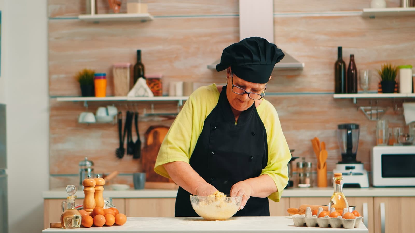 Woman wearing chef bonete while mixing cracked eggs with flour in kitchen while preparing food following traditional recipe.