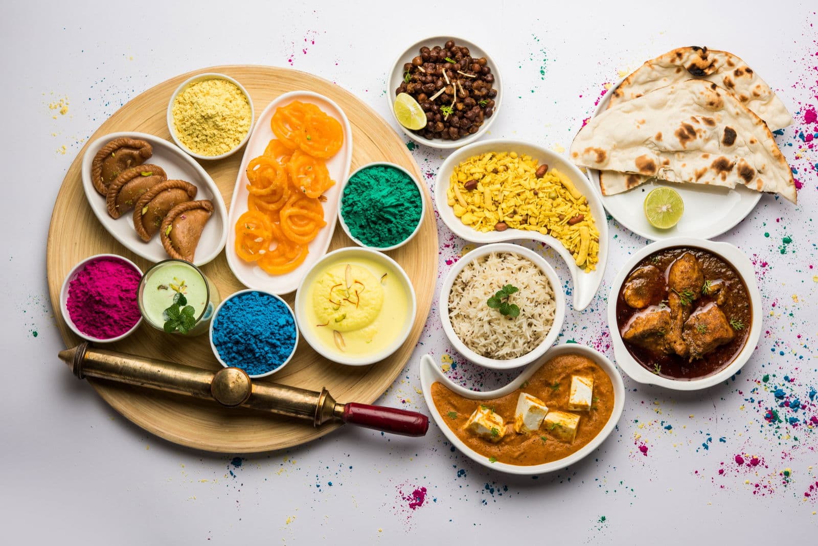 Happy holy concept showing indian assorted lunch food like jalebi ras malai thandai, gujiya and farsan with holi colours and pichkari
