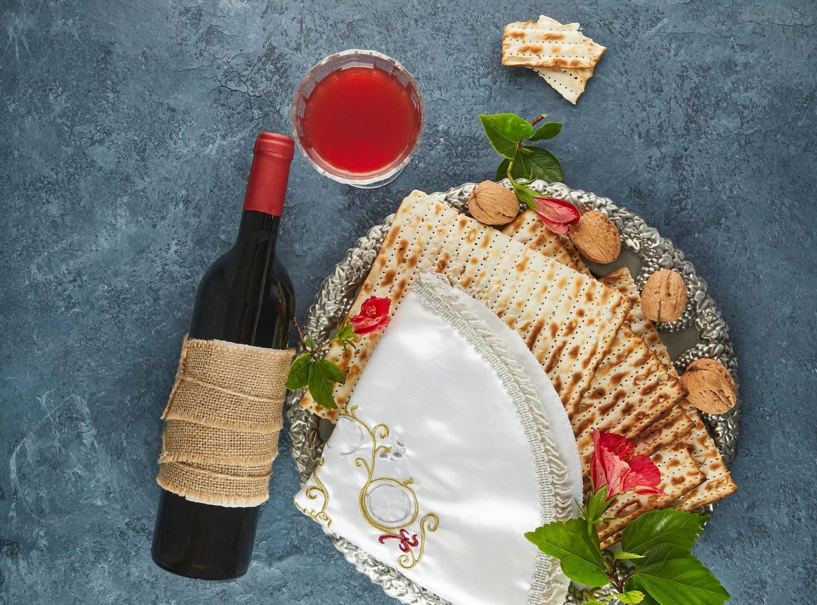 Pesach celebration concept jewish passover holiday matzah on traditional seder plate with bottle of red wine glass of wine nuts and flowers flat lay