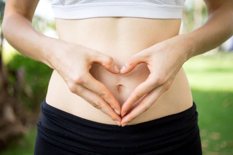 Close-up of a woman forming a heart shape with her hands over her stomach, symbolizing gut health and inflammation reduction.