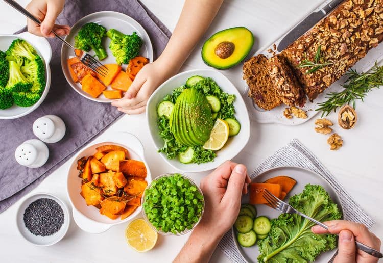 Top view of a colorful and balanced vegan meal with vegetables, avocado, nuts, and whole grain bread