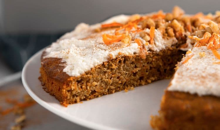 Homemade healthy carrot cake topped with nuts and raisins on a white plate