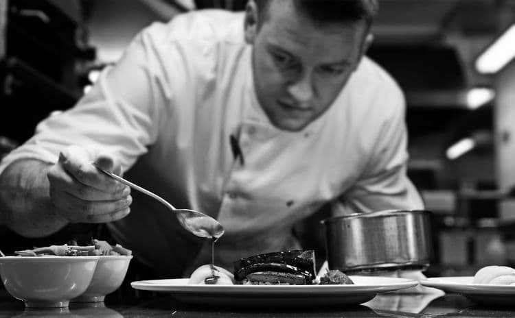 Chef carefully plating a gourmet dish in a professional kitchen, showcasing Michelin-level precision