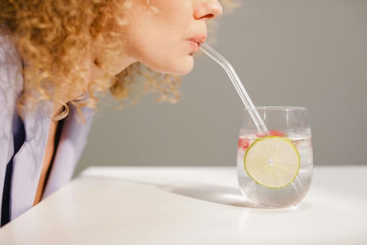 person drinking water with aliced cucumber and some citrus fruit.