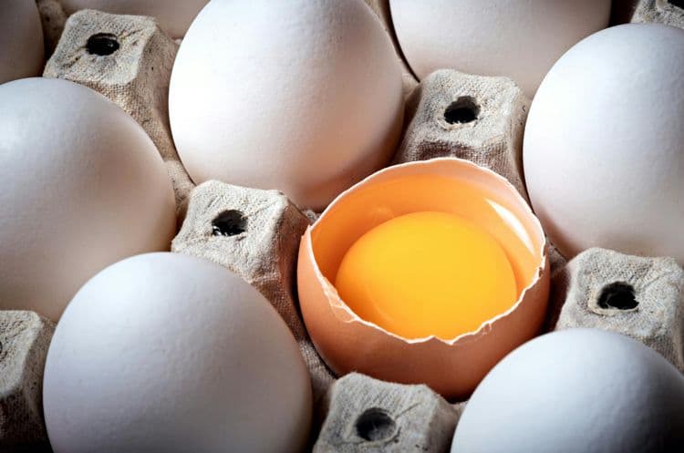 A tray of raw eggs with one cracked open.