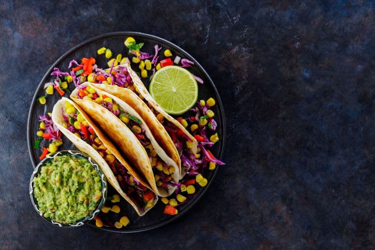 Vegetarian tacos with sweet corn, purple cabbage, and tomatoes on a black plate — vibrant ingredients perfect for recipe storytelling.