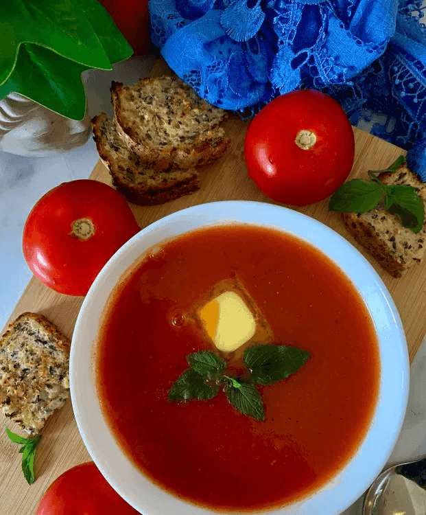 A close-up of tomato soup in a bowl with a slice of butter placed as garnish.