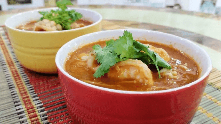A close-up of concentrated tomato seafood soup, with a few pieces of prawns and cilantro leaves placed as garnish.