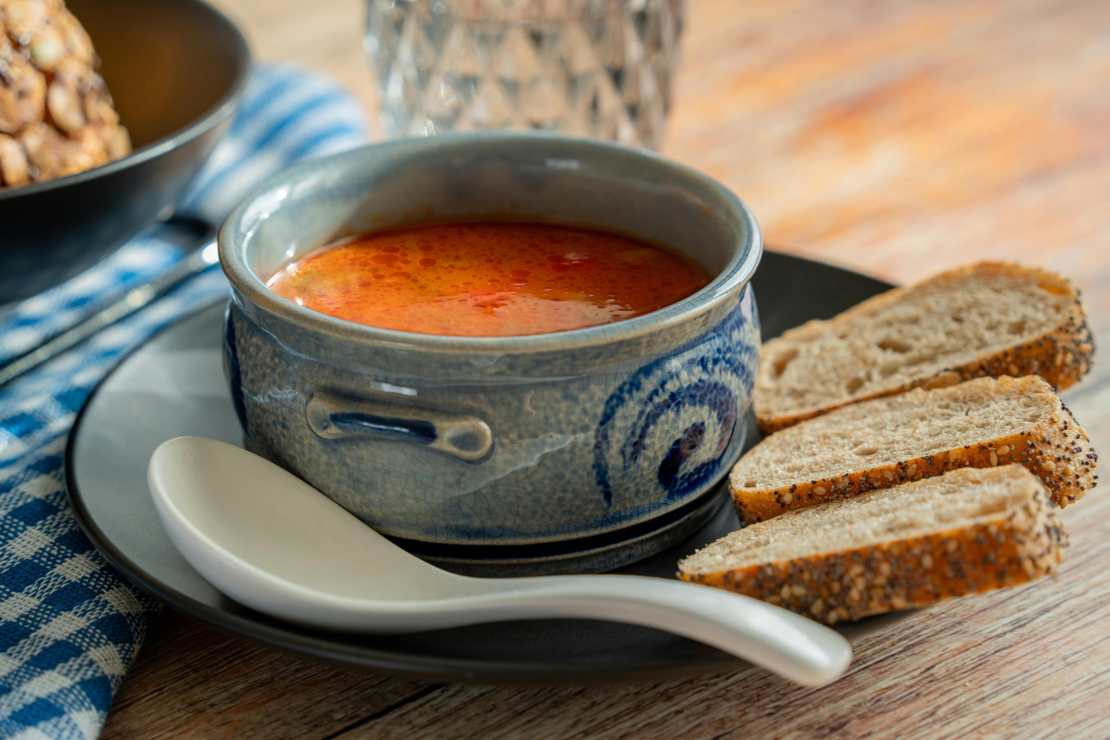 Freshly made soup served in a bowl with some croutons placed beside the bowl as garnish.
