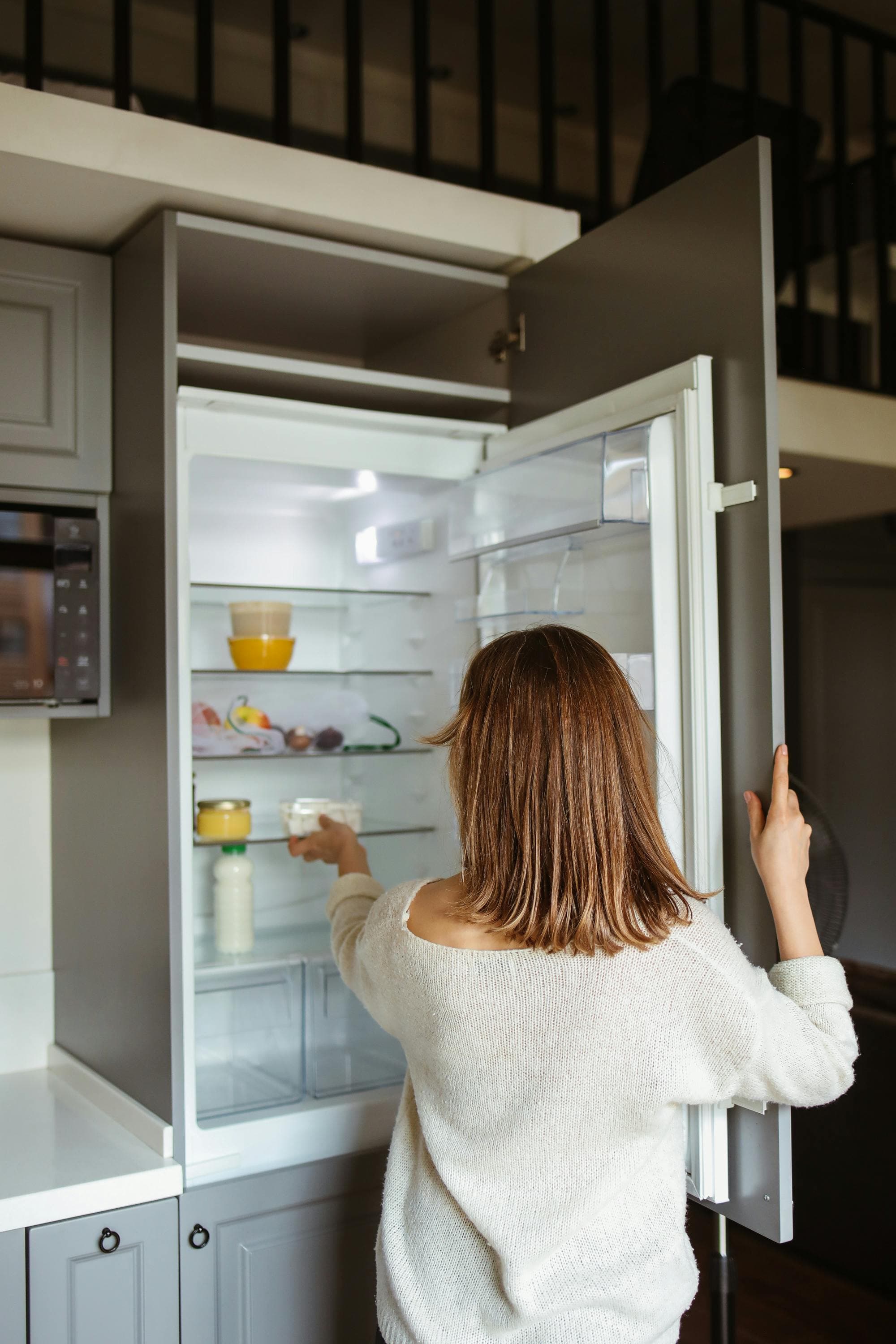 A woman taking a food item out of her home refrigerator.