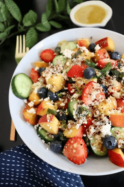 Vibrant bowl of quinoa salad with strawberries, blueberries, peaches, cucumber, mint, and feta—showcasing quinoa as an alternative‑protein breakfast.