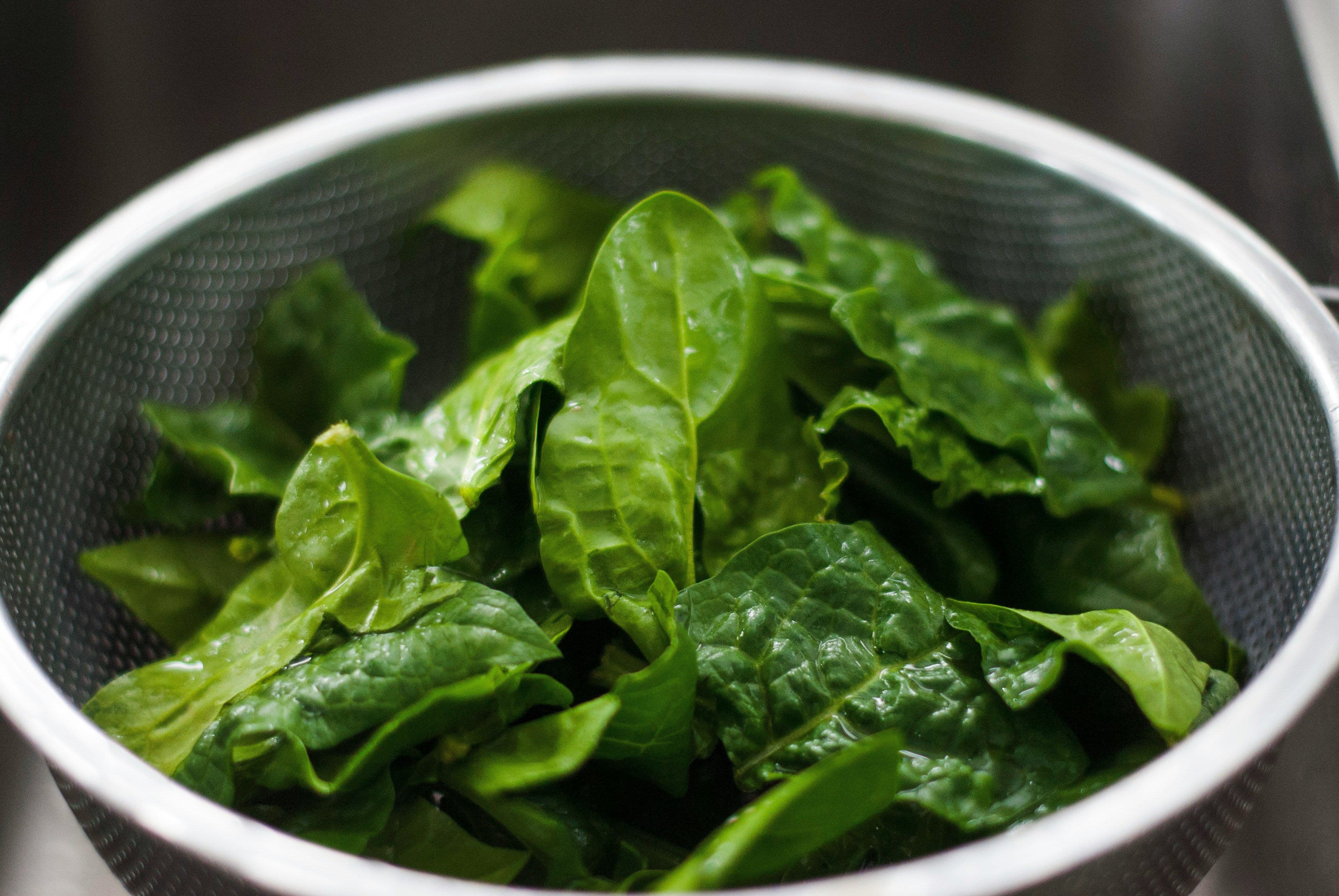 A bunch of raw spinach leaves placed in a strainer.