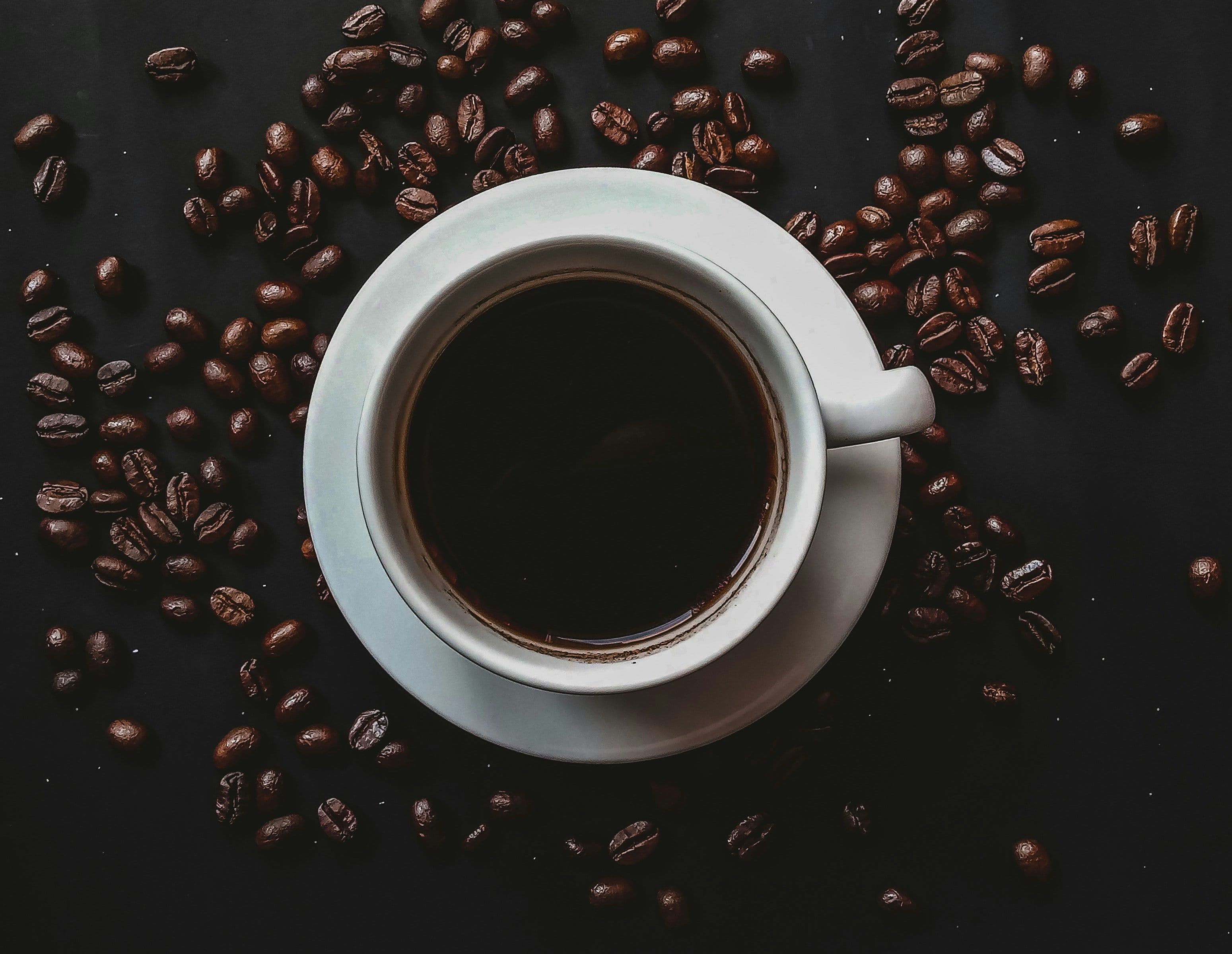 A cup of black coffee placed in the center with several coffee beans lay scattered around it.
