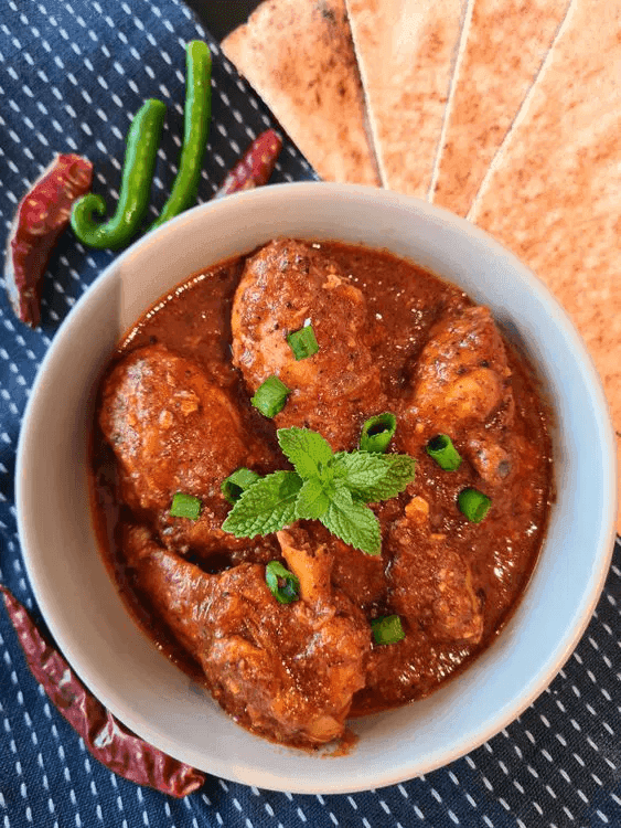 A close-up of a plate containing chicken vindaloo garnished with mint leaves and chopped green onion.