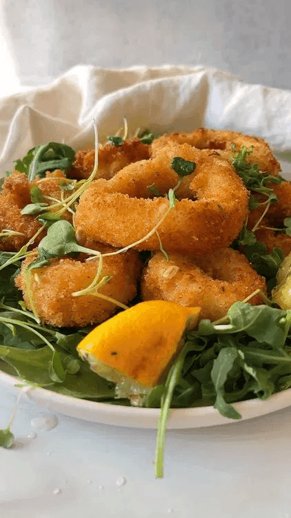 A close-up of a plate containing fried calamari alongside some fresh greens.