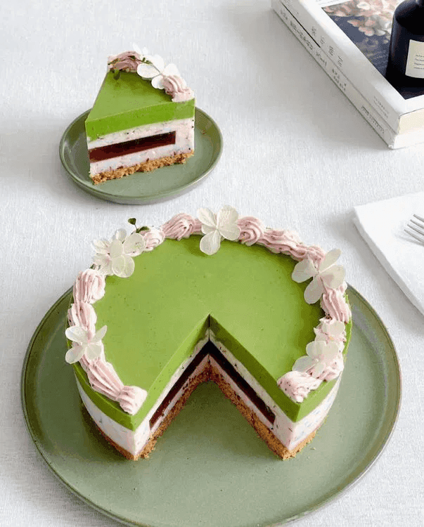 A piece of Bayberry Matcha Cheese Mousse and the remaining whole cake placed beside each other on two separate plates.