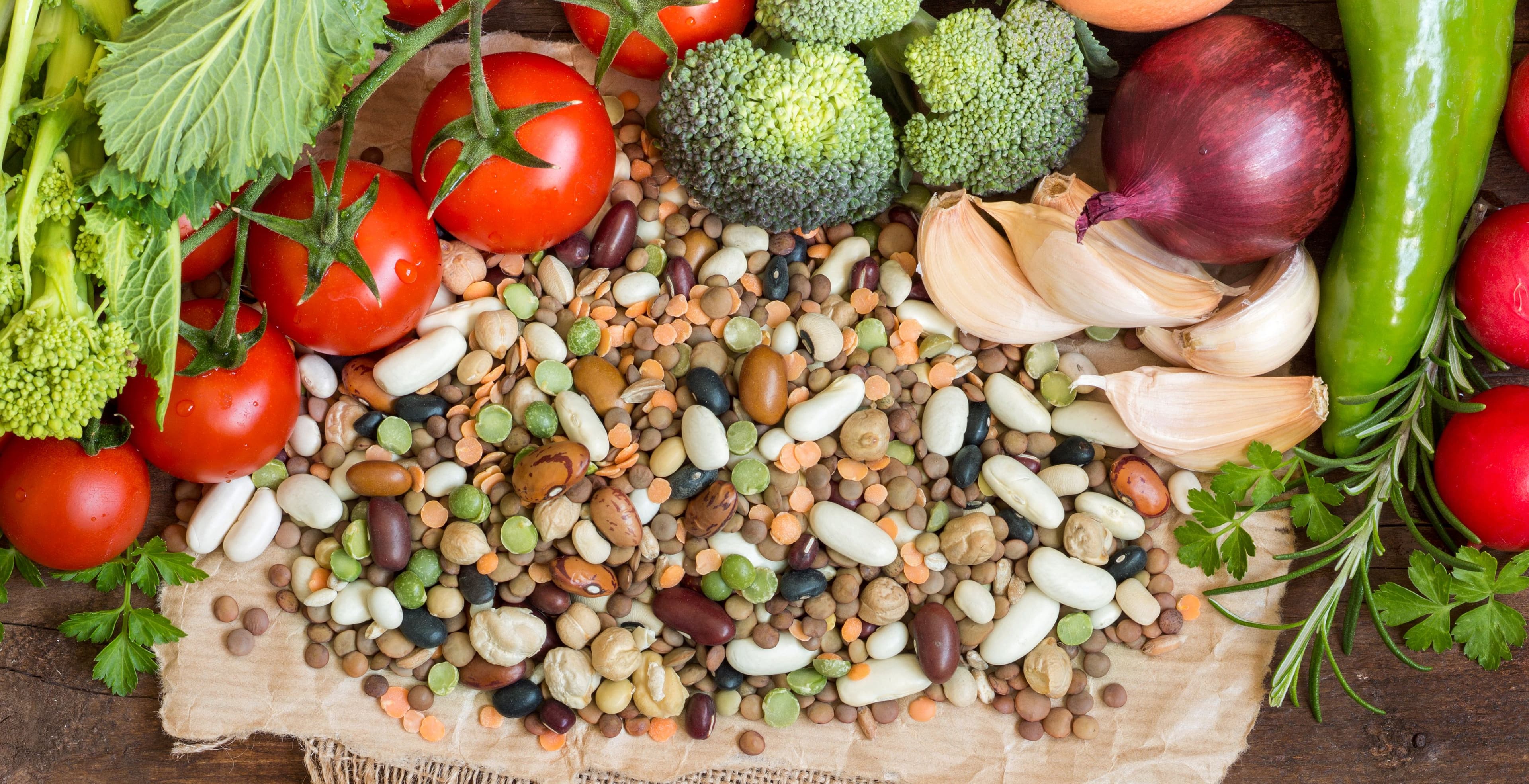 A colorful assortment of fiber-rich foods, including legumes, tomatoes, broccoli, garlic, and leafy greens.