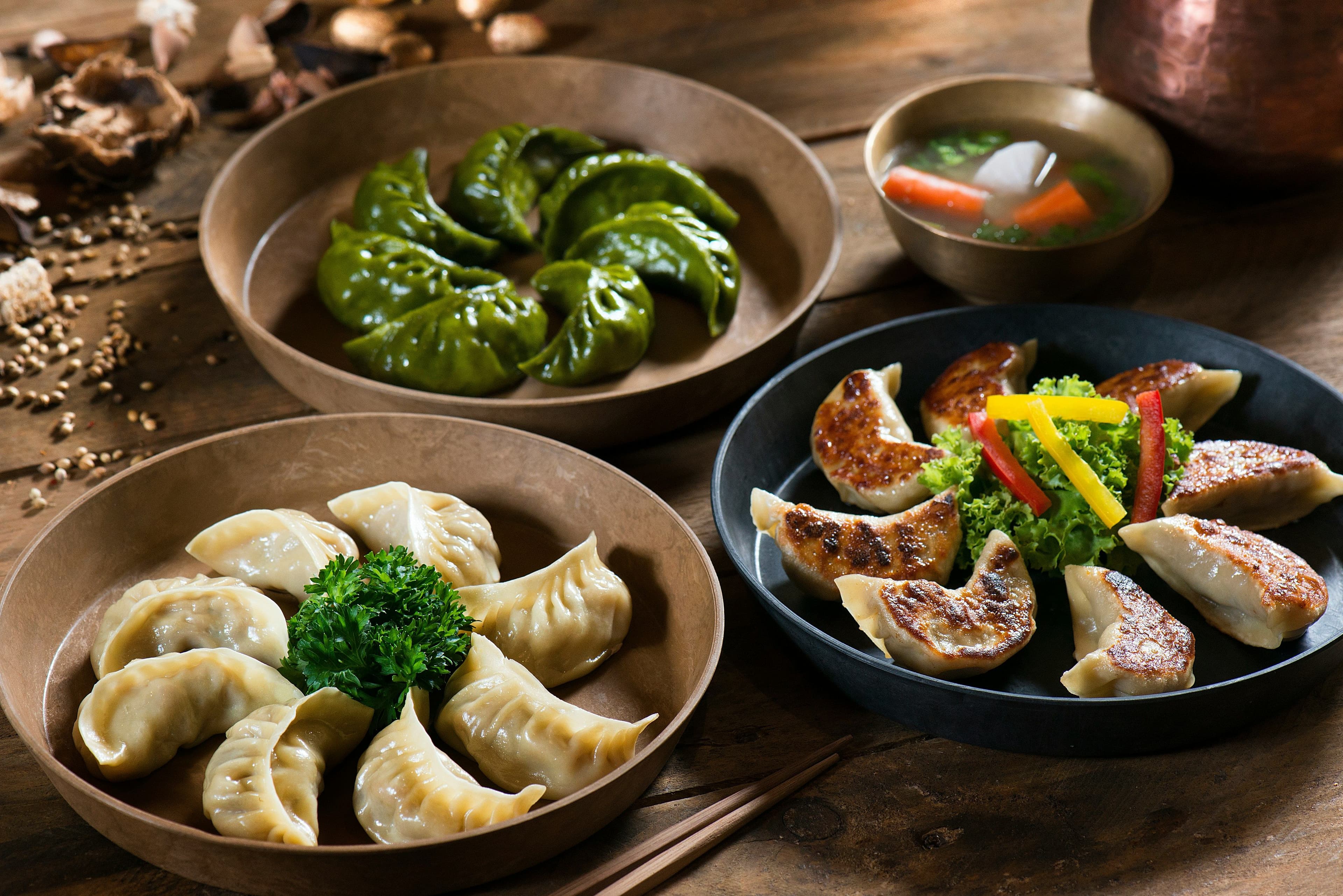 Several plates with different types of dumplings placed on a wooden table.