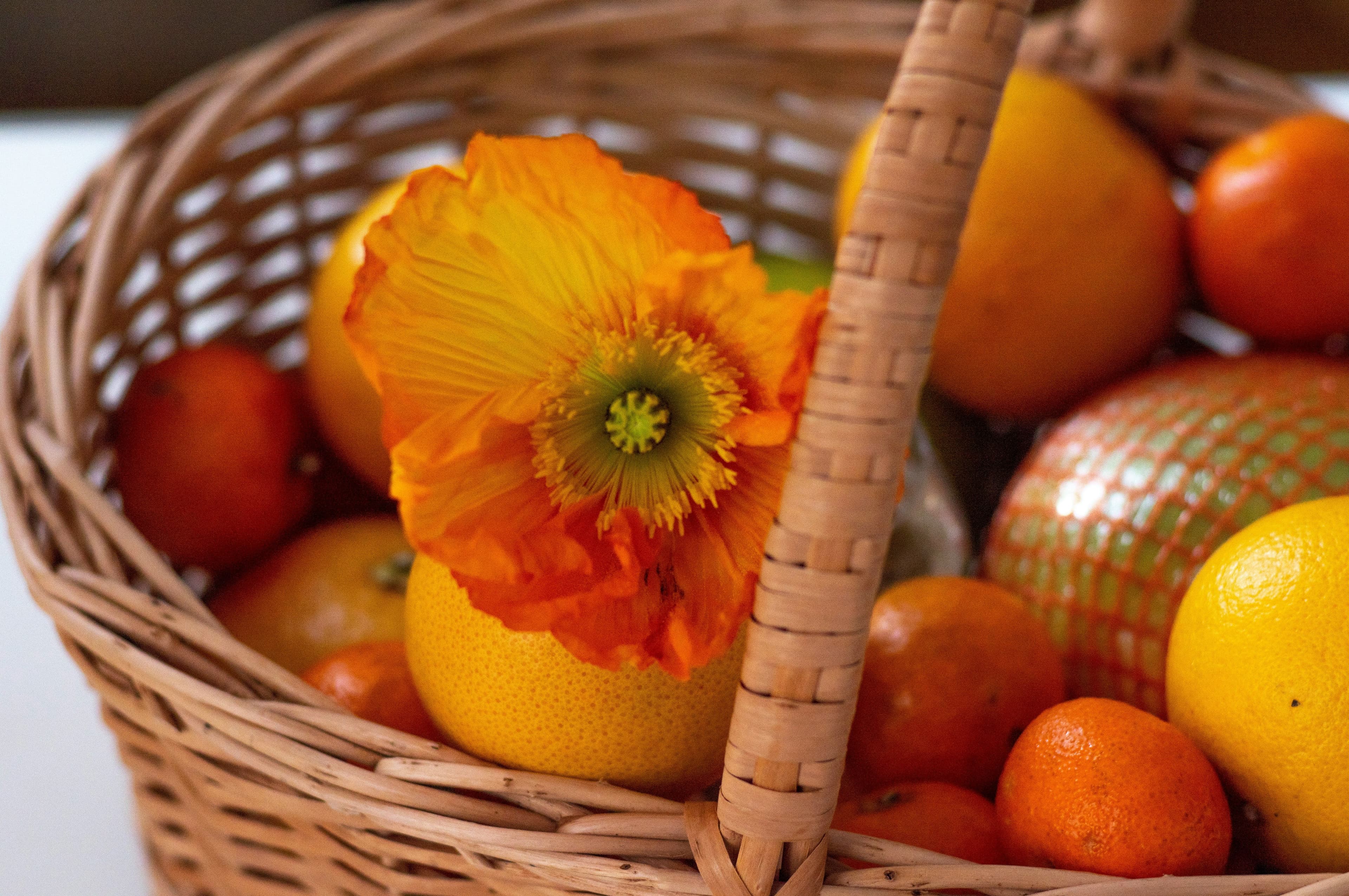 Oranges placed in a basket alongside an orange colored flower.