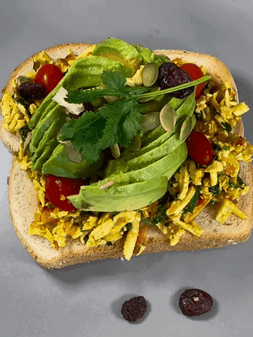 Open‑face toast topped with tofu scramble, sliced avocado, cherry tomatoes, pumpkin seeds, and cilantro—an alternative‑protein vegan breakfast.