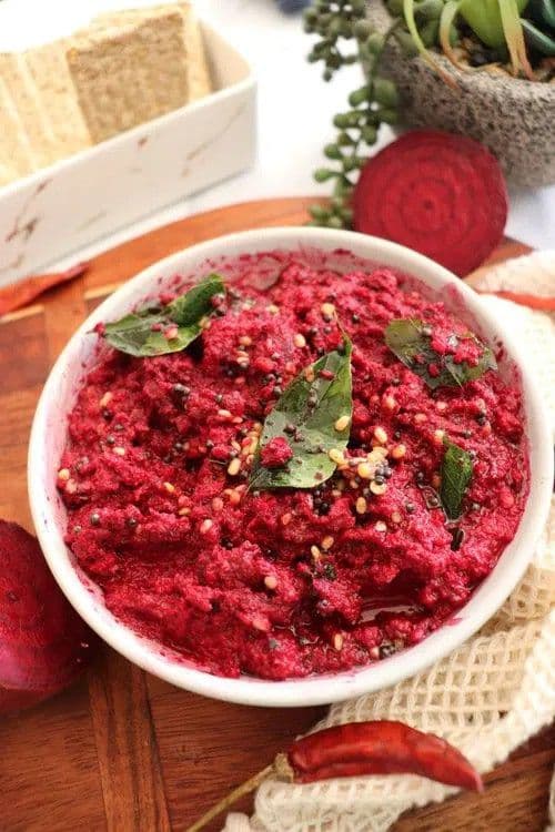 A close-up of freshly made Beetroot Chutney placed in a bowl with a curry leaf on top and a red chilli placed beside the bowl.