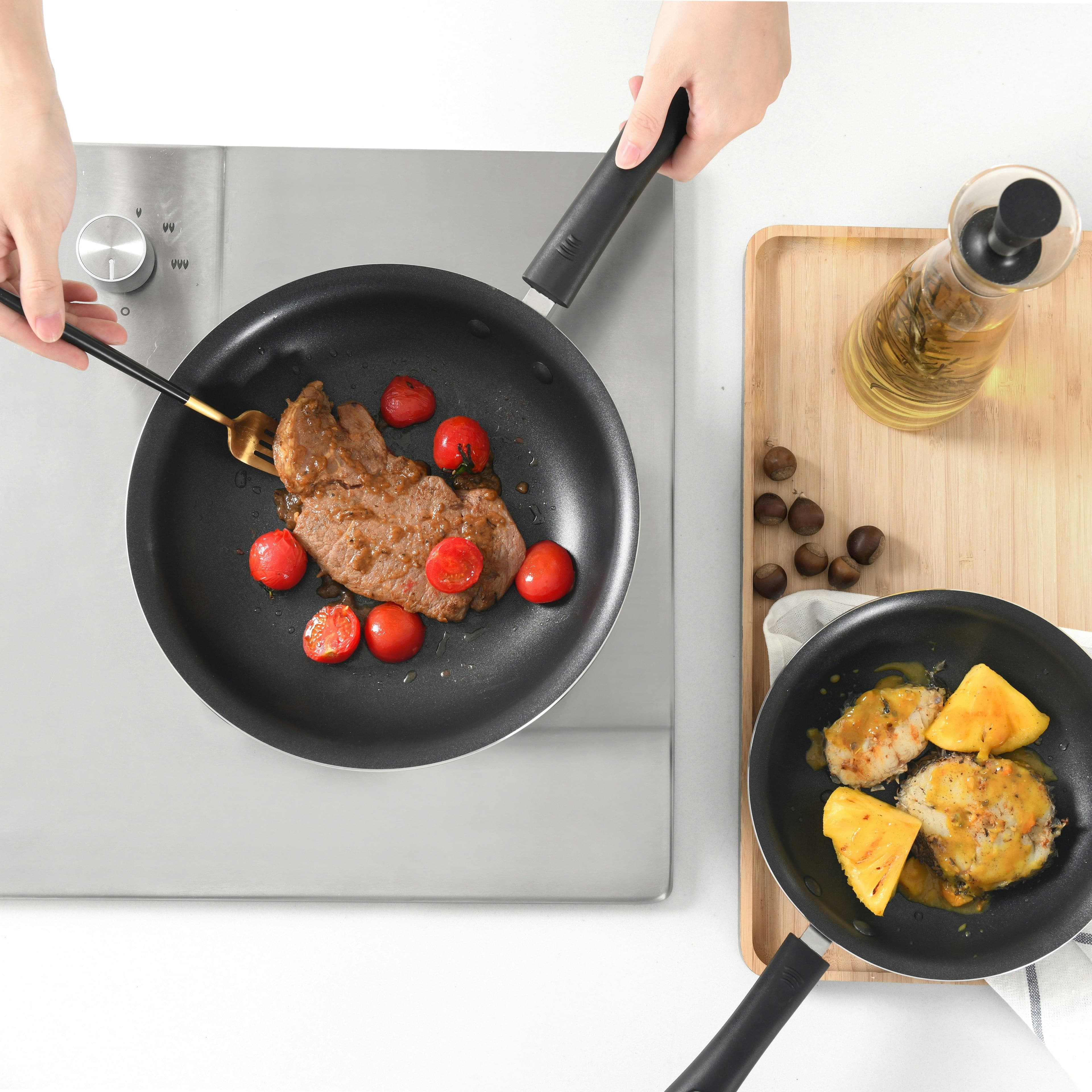 Steak with some tomatoes being cooked in a non-stick pan.