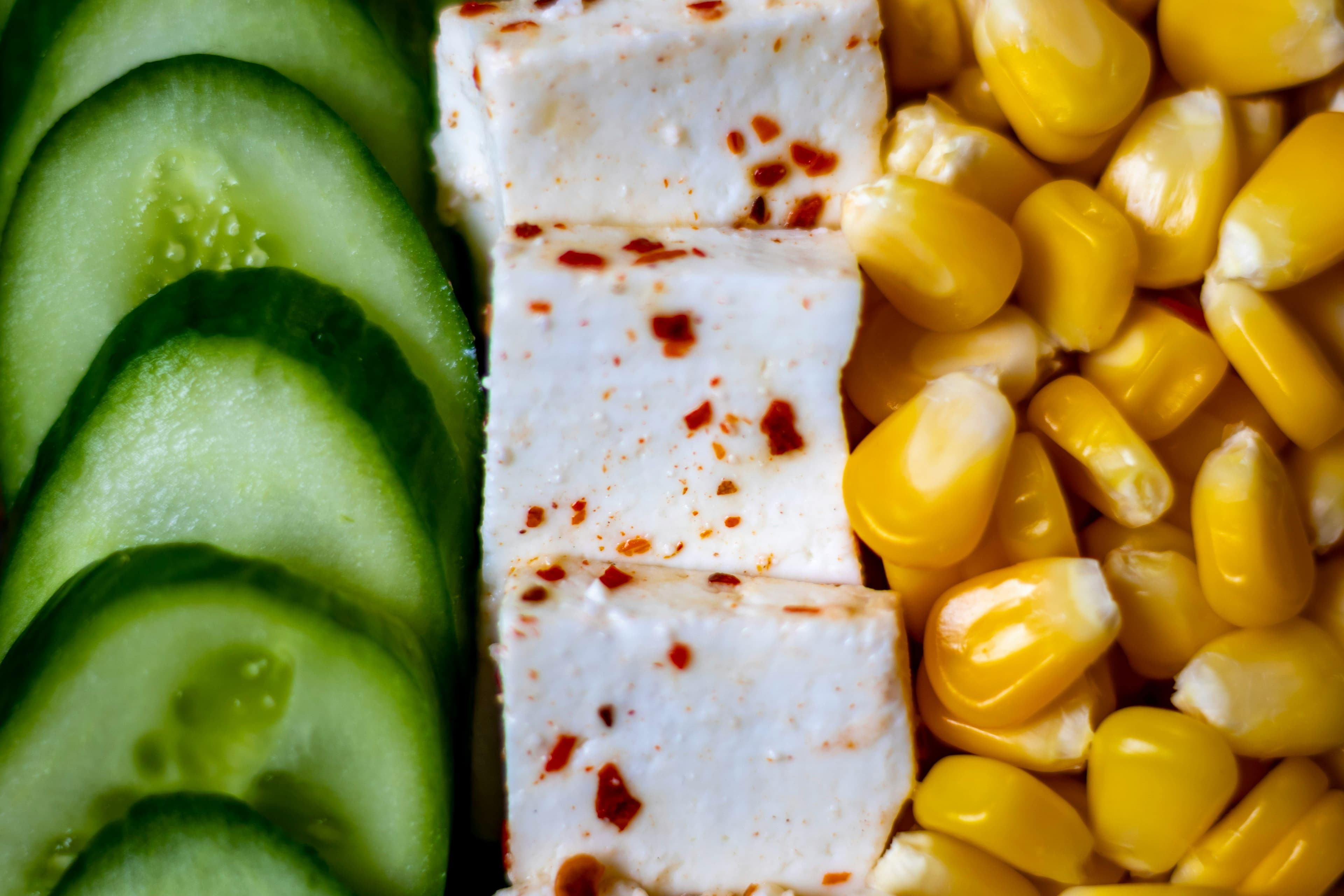Tofu placed in a straight row with corn and cucumbers on both sides.
