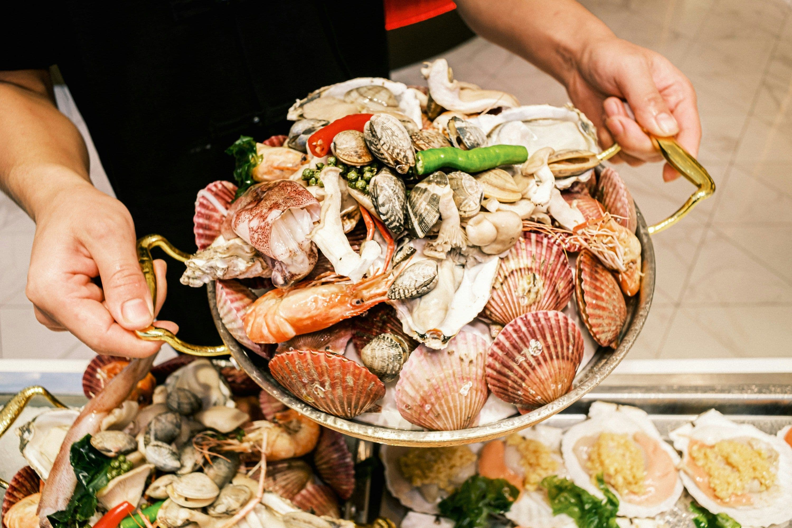 A man is holding a utensil filled with different kinds of seafood.