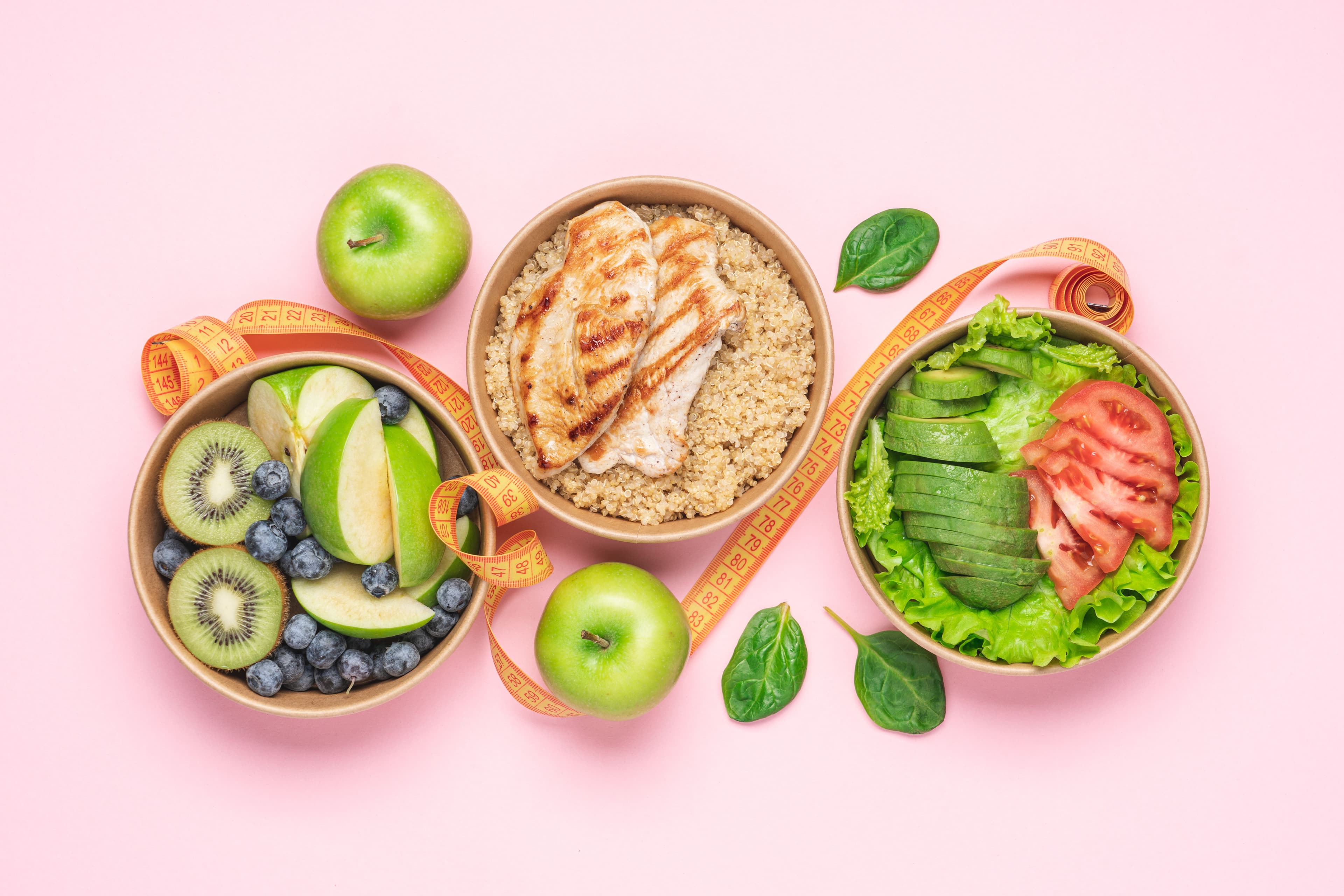 Balanced healthy meal with avocado salad, quinoa, chicken breast, and berries on a vibrant pink background