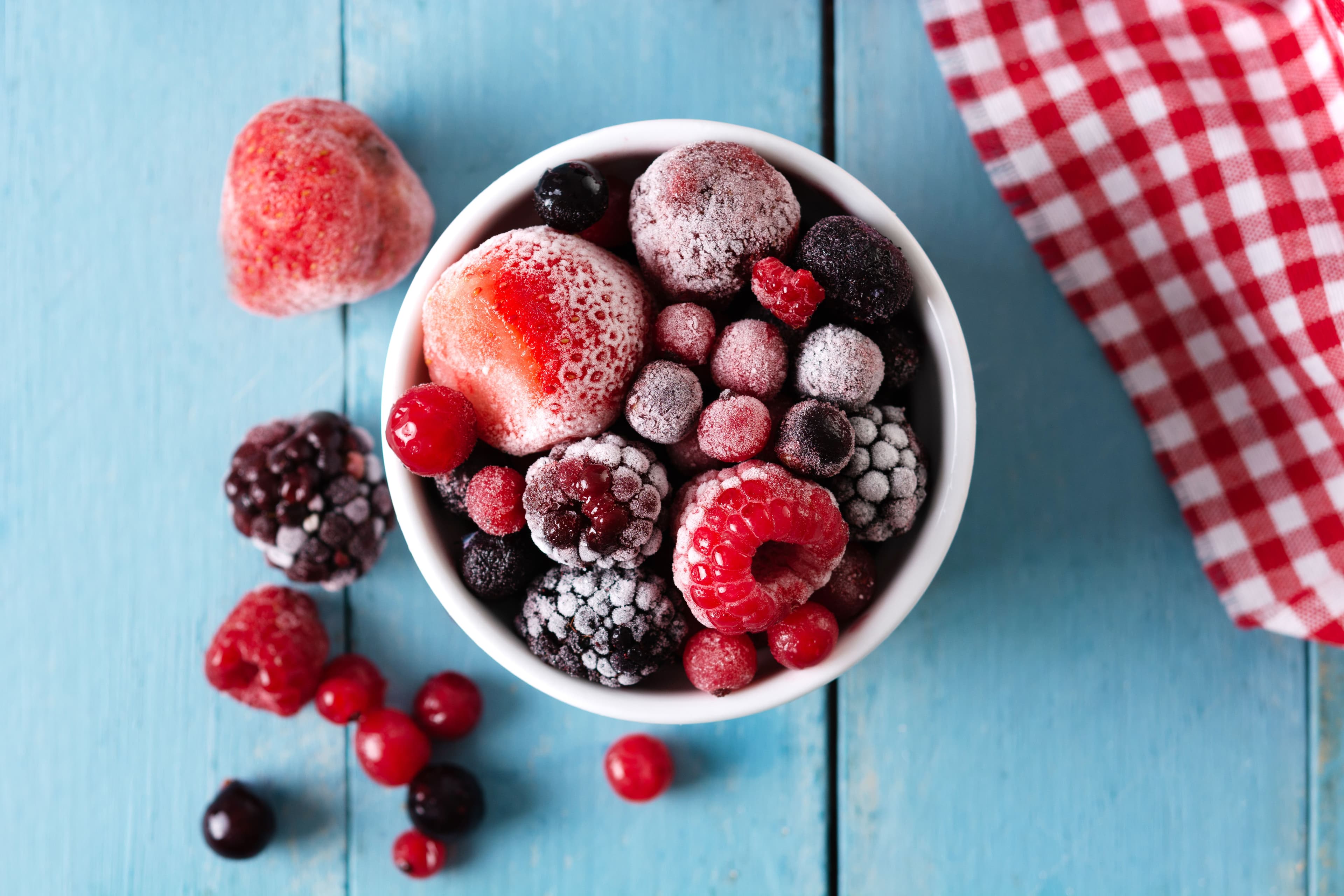Close-up of a bowl filled with iced blueberries, raspberries, and blackberries on a blue wooden table.