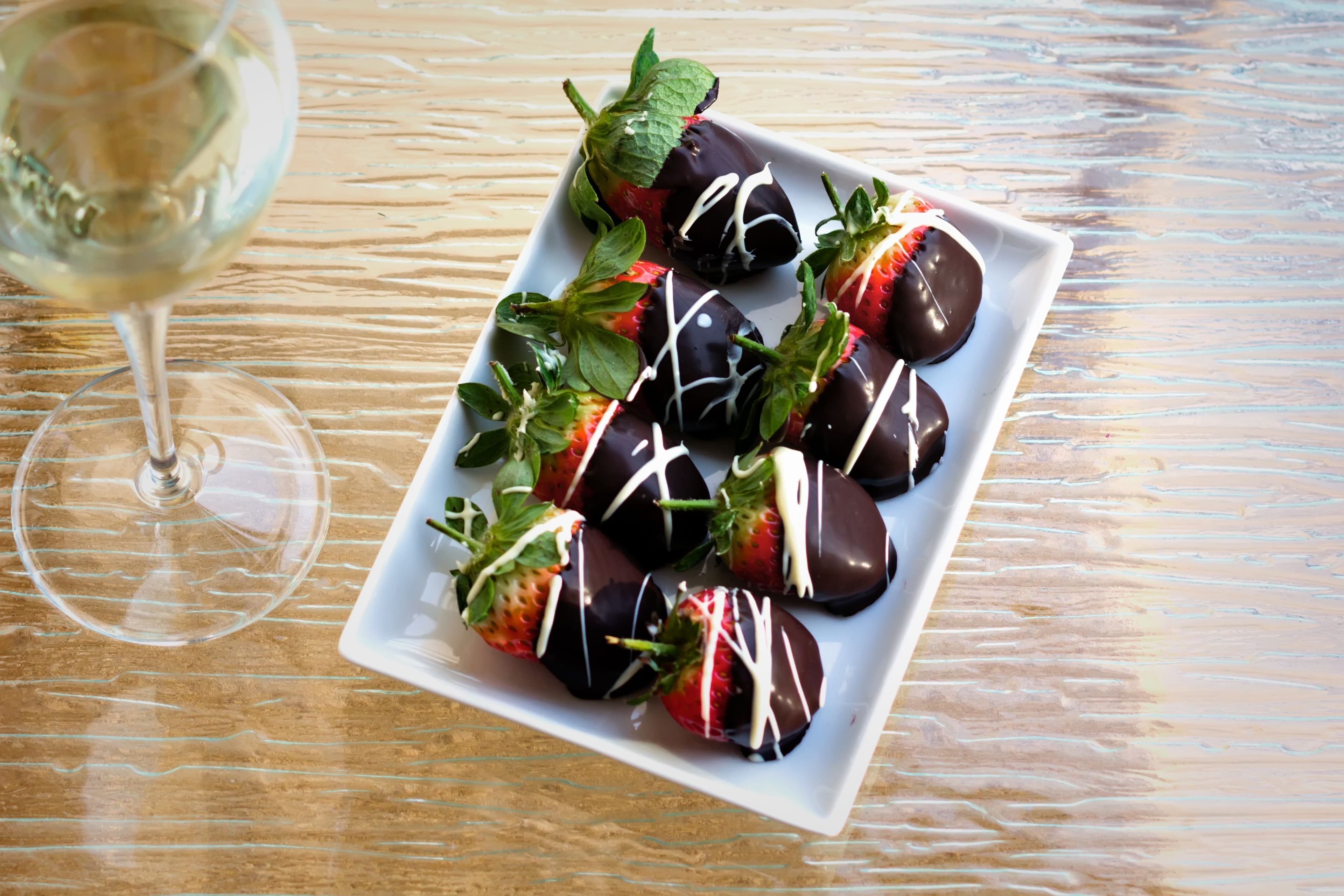 Several chocolate covered strawberries laid out on a rectangular white plate
